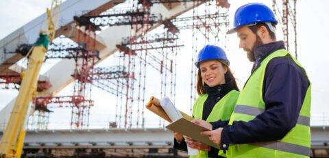 Teamwork-in-construction-industry---two-engineers-working-together-on-construction-site-with-blueprints-and-plans-645373486